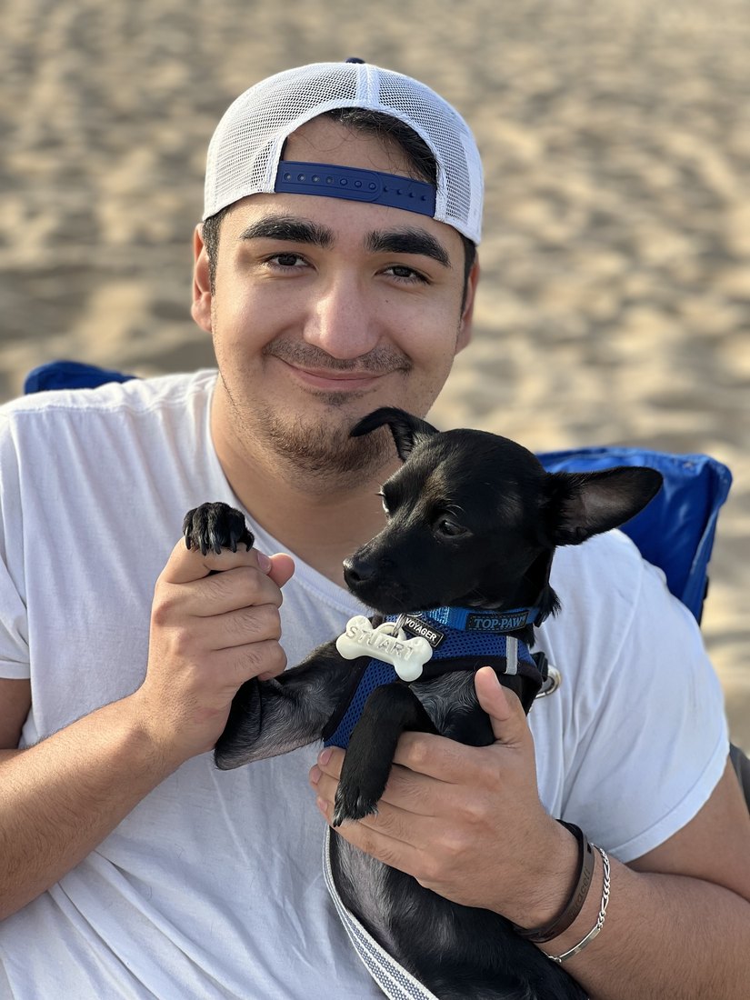 Andy Hernandez holding Stuart, his small black Chihuahua, at the beach
